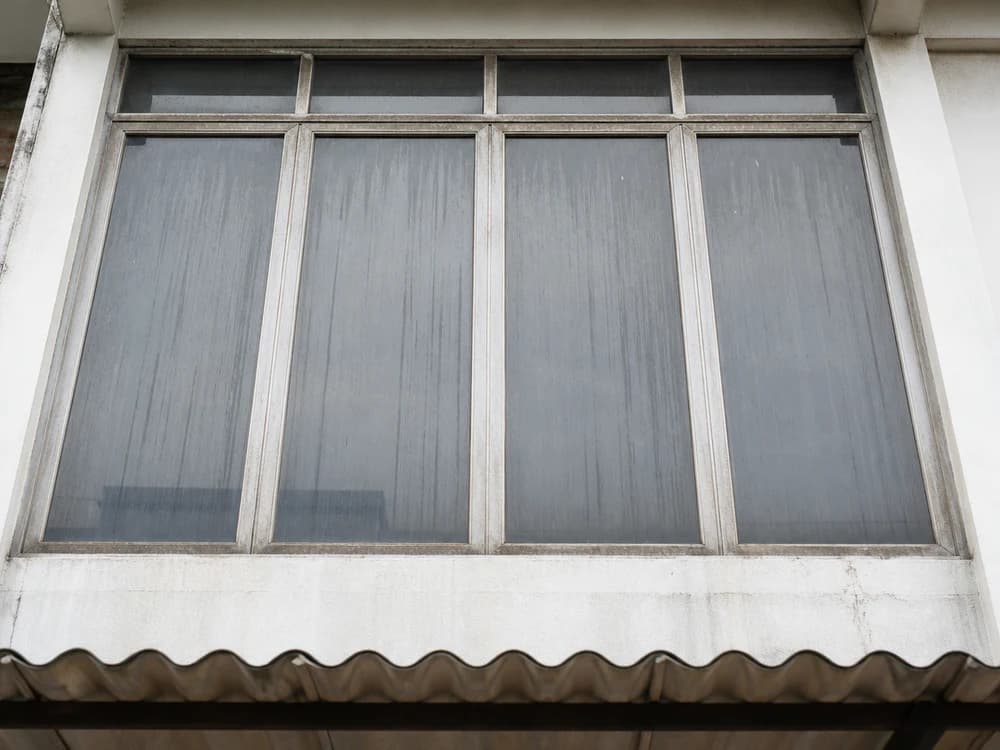 Upper-floor shop glass — rain streaks and built-up dust