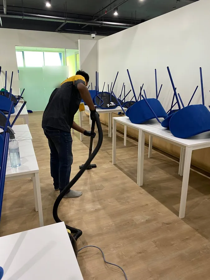 Yellowbee crew member vacuuming between office tables with chairs placed on top