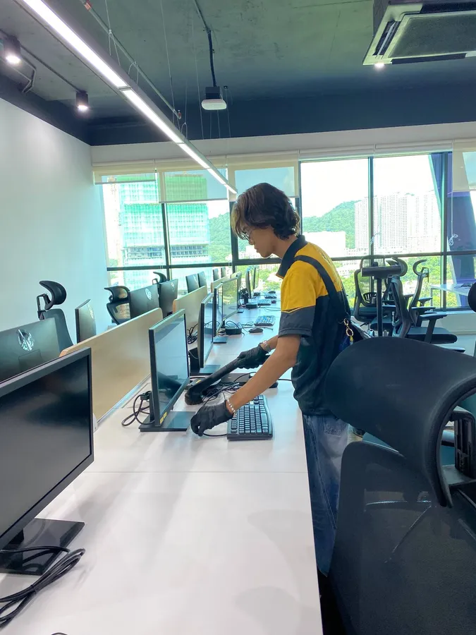 Yellowbee crew member vacuuming the desk beside a keyboard in an open-plan office