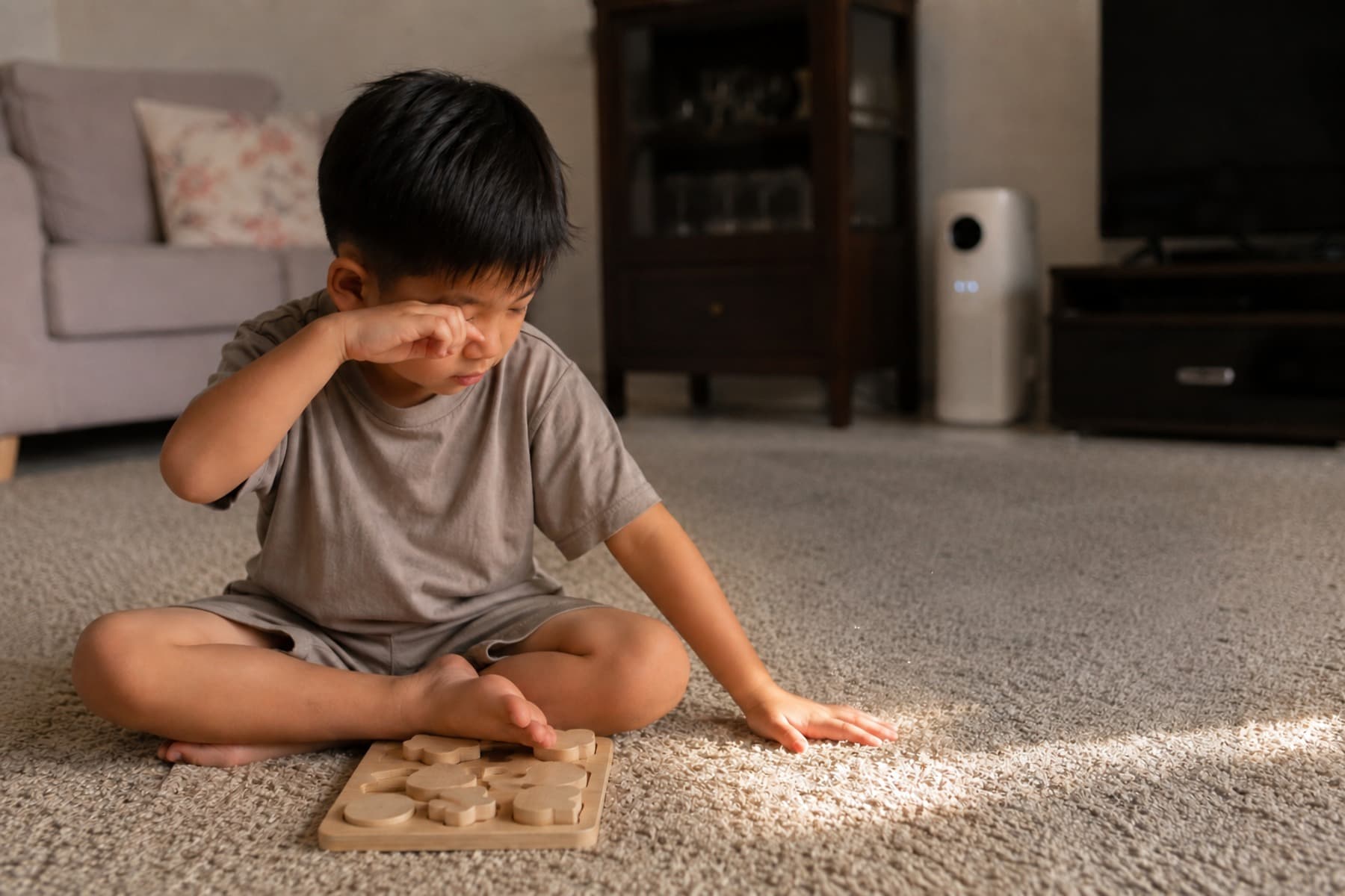 Child rubbing his eye while dust rises from the carpet where his hand presses down