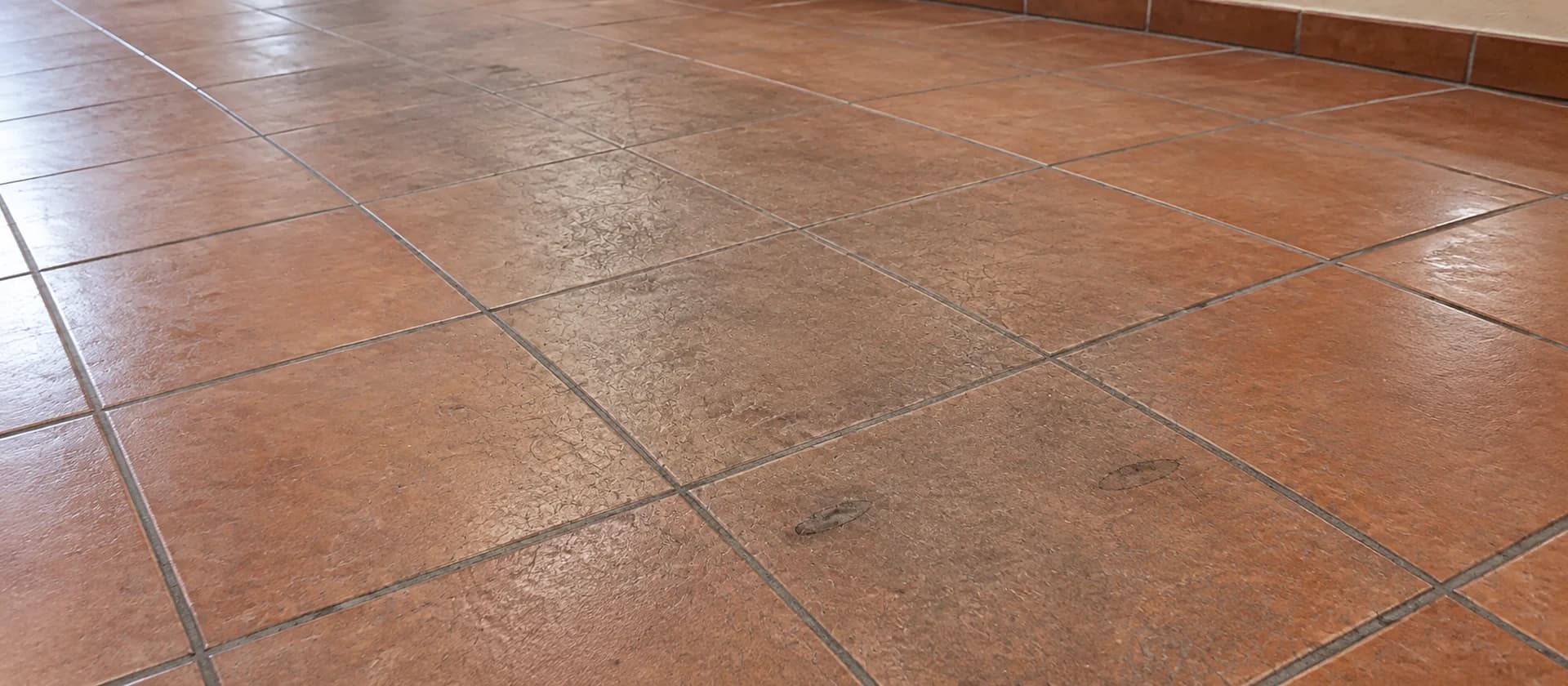 Reddish-brown floor tiles showing a dull, worn traffic lane and scuff marks