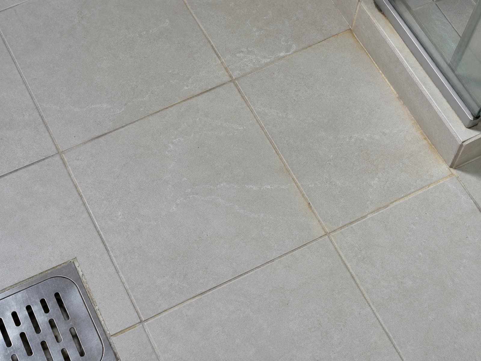 Faint white marks on grey bathroom tiles and yellowish grout beside a shower screen and floor drain
