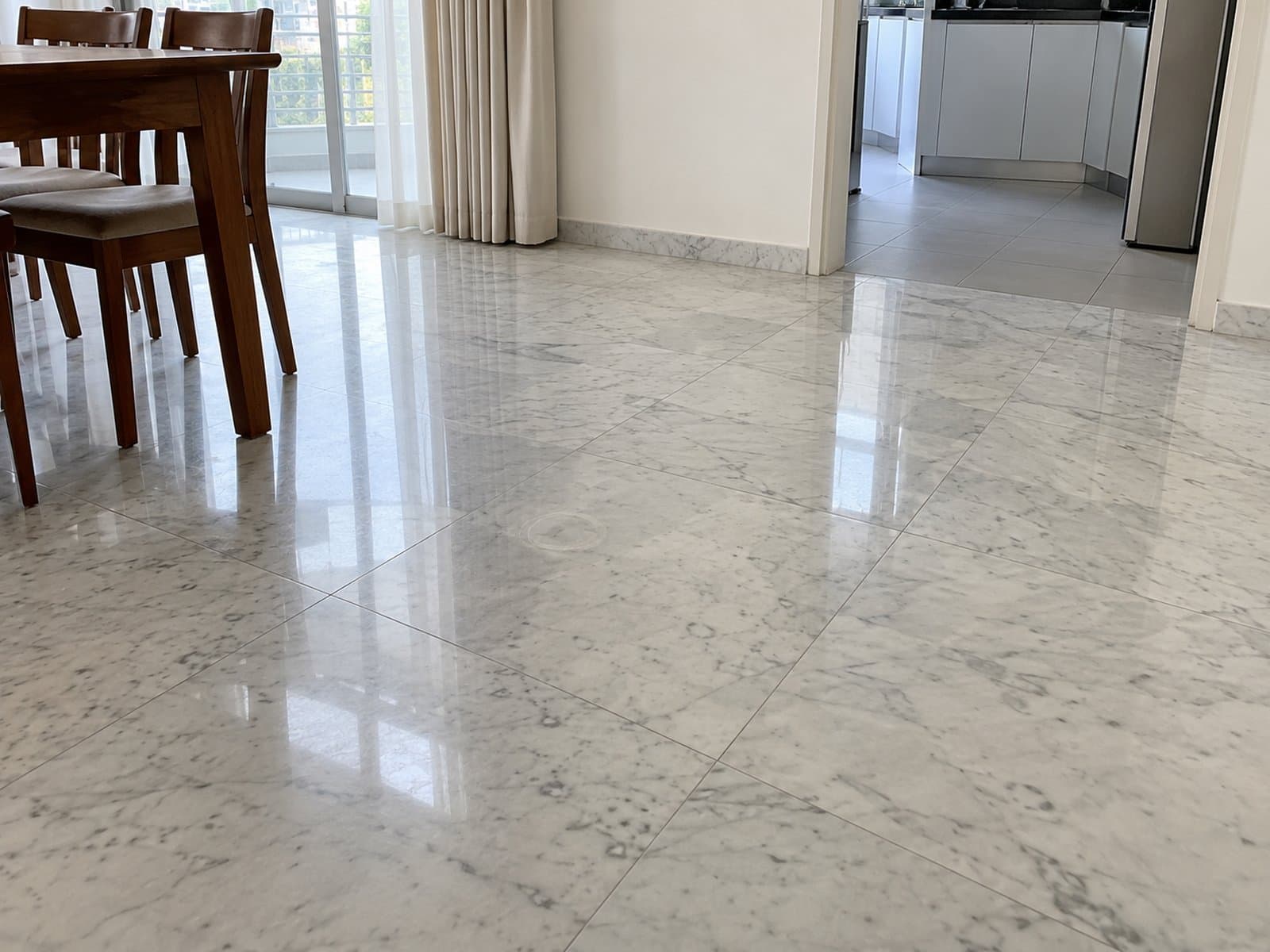 Glossy grey-veined floor beside a wooden dining table, with a tiled kitchen through an open doorway