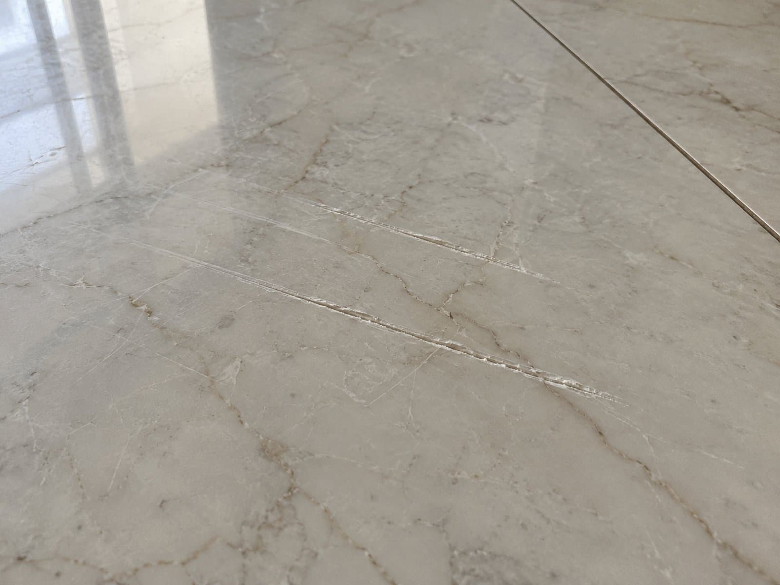 Several long scratches with pale, rough edges across glossy veined stone flooring