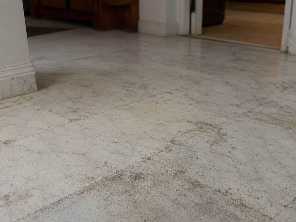 Marble floor surface showing dull, etched patches from acid exposure