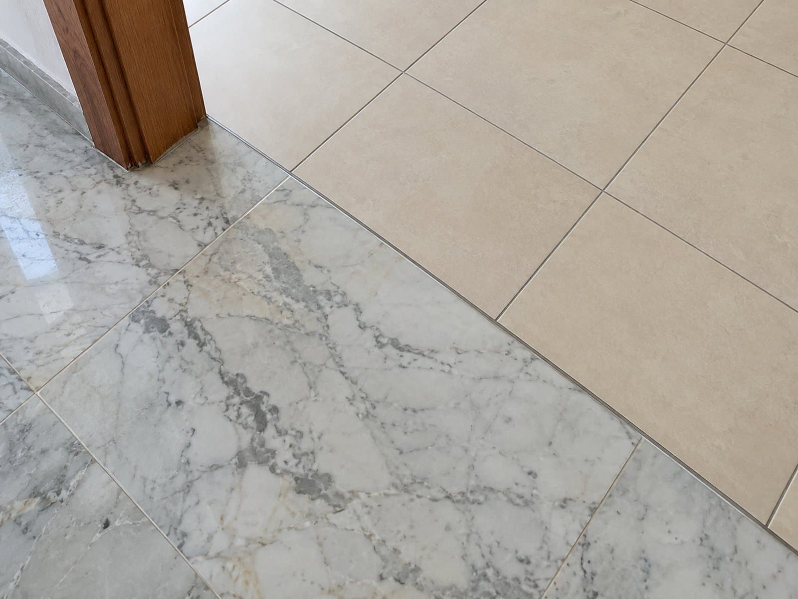 Grey-veined stone flooring meets beige square tiles along a straight threshold beside a wooden door frame